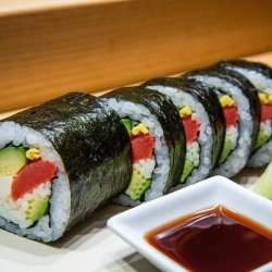 A plate of various sushi, including California rolls and gimbap, arranged neatly on a tray. The sushi features rice wrapped in nori with slices of fish and vegetables, showcasing the art of Japanese cuisine. The setting is indoors with a focus on the colorful presentation of the dish.