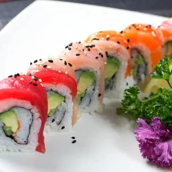 A colorful assortment of freshly prepared sushi rolls on a white plate, featuring vibrant slices of tuna, salmon, and avocado, garnished with sesame seeds and accompanied by parsley and lemon slices. Perfect for Japanese cuisine enthusiasts seeking a visually appealing and delicious dining experience.